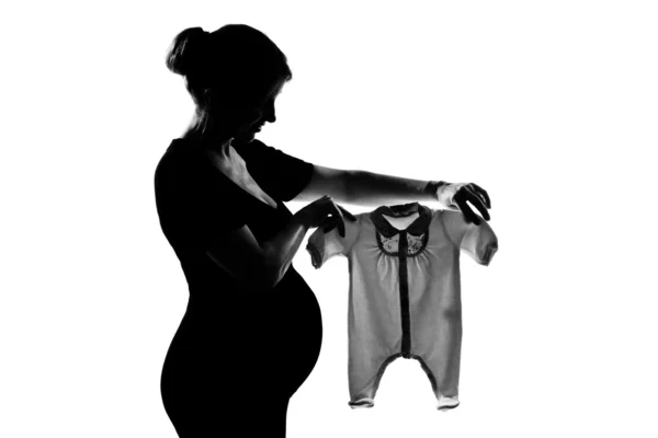 Μια έγκυος γυναίκα, κρατώντας τα ρούχα του μωρού — Φωτογραφία Αρχείου