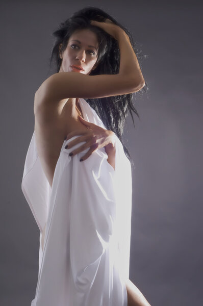 Nude female body against dark background with white sheet