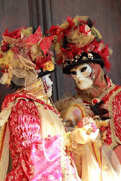 Vermelho e ouro casal mascarado contra a porta de madeira — Fotografia de Stock