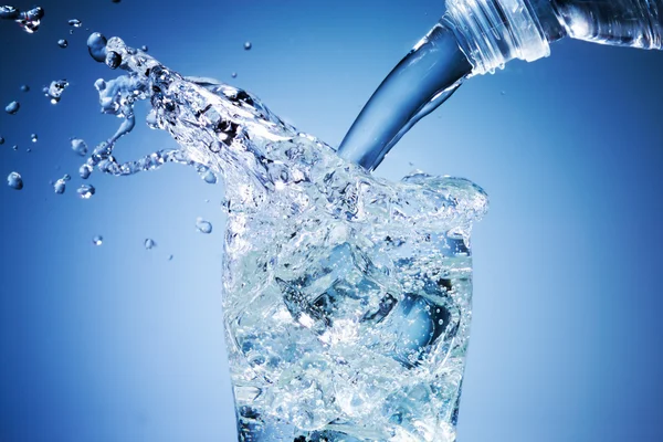 Wasser ergießt sich in Glas auf blauem Hintergrund — Stockfoto