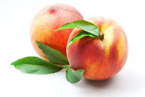 Zwei reife Pfirsichfrüchte mit grünen Blättern isoliert auf weiß — Stockfoto