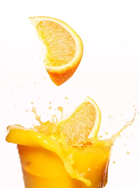 As partes de laranja caem no suco. vidro sobre fundo branco — Fotografia de Stock