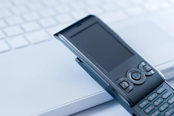 Mobiltelefon på vita laptop tangentbord — Stockfoto