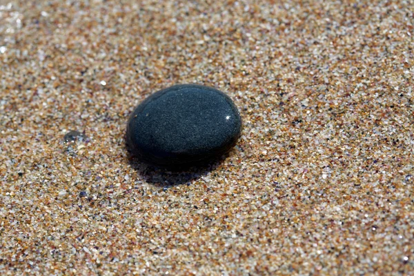 Black SPA stone on sea sand — Stock Photo, Image