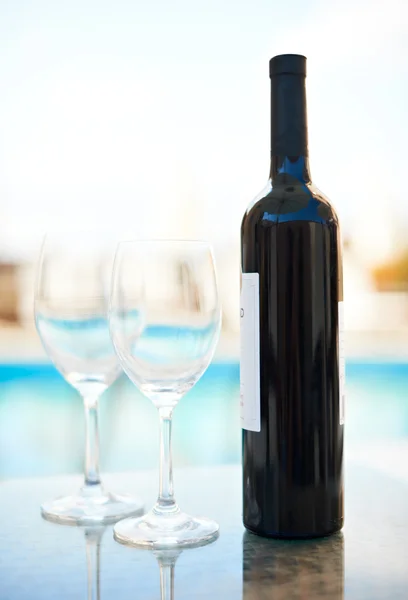 Rött vin och glasögon nära blå vatten — Stockfoto
