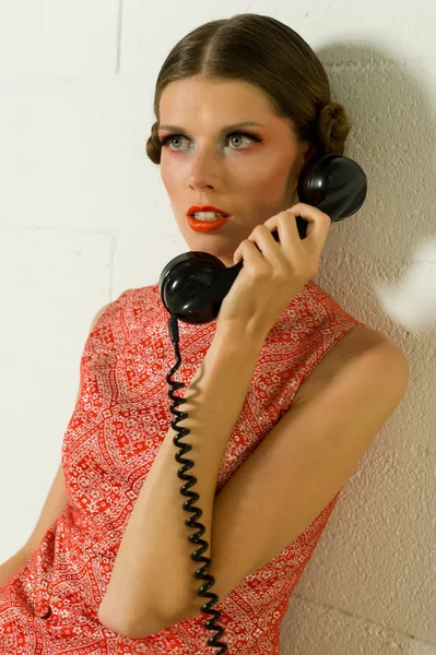 Menina chamando em um telefone antigo vestido de laranja em um sofá — Fotografia de Stock