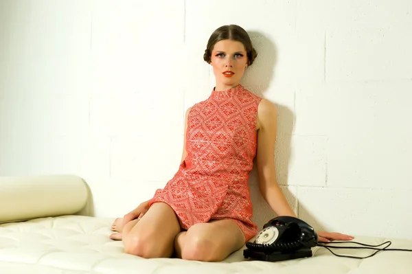 Ragazza che chiama su un vecchio telefono vestito di arancione su un divano — Foto Stock