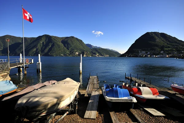Lugano lake met swiss vlag en boten — Stockfoto