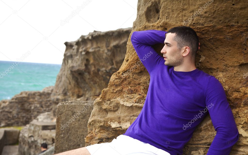 Man laying on the rocks on the beach looking toward the sunlit water pensiv