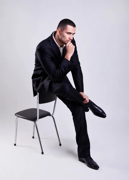 Κομψό νεαρό επιχειρηματία που κάθεται σε μια καρέκλα, πέρα από το γκρι φόντο — Φωτογραφία Αρχείου