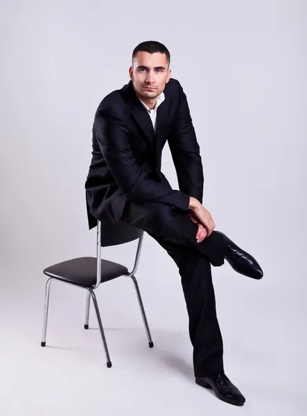 Κομψό νεαρό επιχειρηματία που κάθεται σε μια καρέκλα, πέρα από το γκρι φόντο — Φωτογραφία Αρχείου