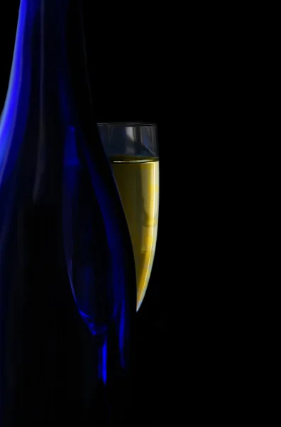 Glass of champagne and blue bottle, on black — Stock Photo, Image
