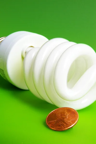 Light bulb and penny, closeup on green background — Stock Photo, Image