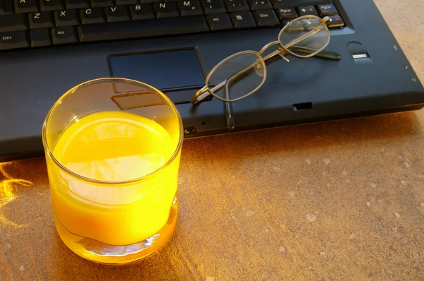 Szklanki soku pomarańczowego rano z laptopa i okulary — Zdjęcie stockowe
