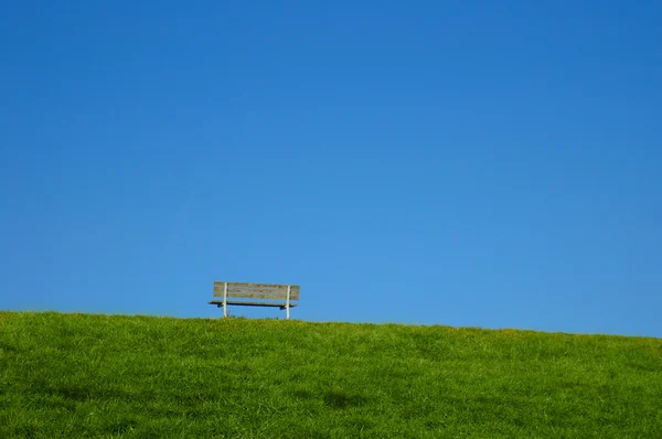 Bench on a hill with green grass and blue sky — Stock Photo, Image