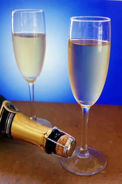 Dwa kieliszki do szampana i butelka na niebieskim tle — Zdjęcie stockowe