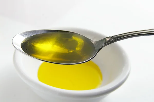 Ложка, полная оливкового масла, над белой чашей — стоковое фото