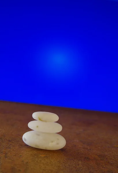 Pedras brancas lisas balanceando contra fundo azul inclinado — Fotografia de Stock