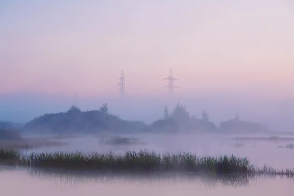 Línea de transmisión en la colina que atraviesa el pantano en la niebla — Foto de Stock