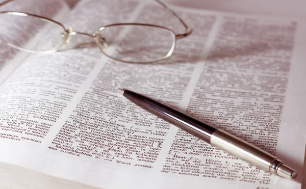 Glazen met pen op het boek — Stockfoto