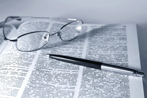 Öppna bok med glasögon och penna — Stockfoto