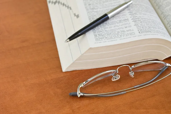 Открытый словарь с очками и ручкой — стоковое фото