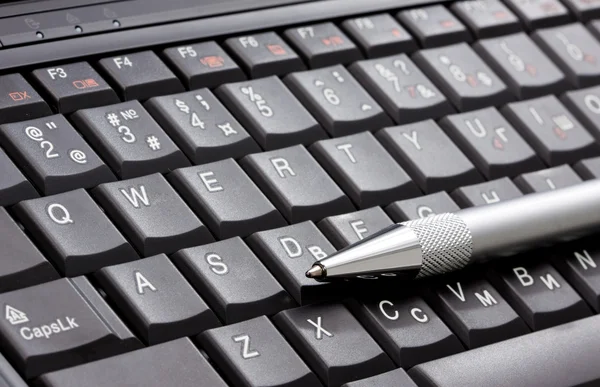 Svart laptop och silver penna — Stockfoto