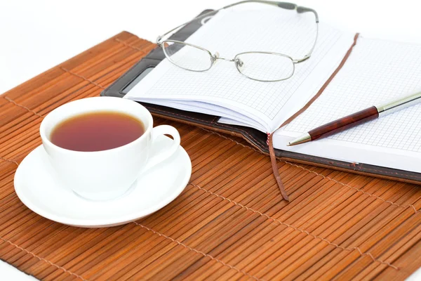 Xícara de chá com caderno, óculos e caneta — Fotografia de Stock