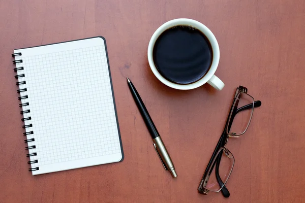 Στυλό, λευκό σπειροειδές σημειωματάριο και γυαλιά με το φλυτζάνι του καφέ — Φωτογραφία Αρχείου