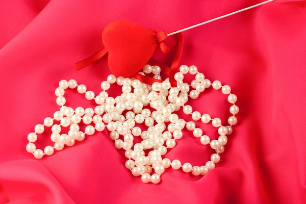 Collar de perlas con corazón rojo sobre seda roja —  Fotos de Stock