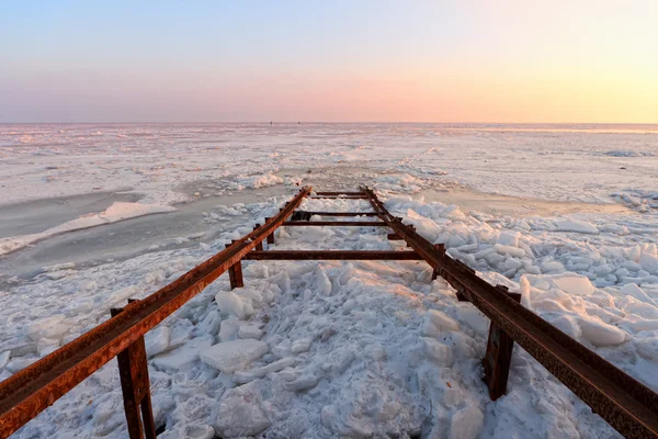 Frozen sea with broken pier at sunset — Stock Photo, Image