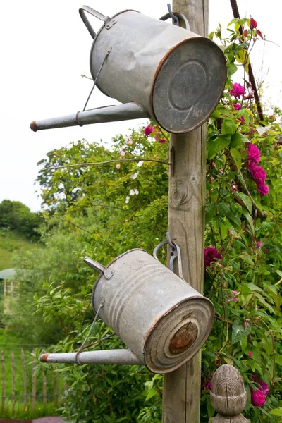 Two watering cans hanging on a wooden pole — Stock Photo, Image