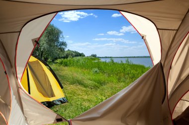 View looking out of door of sun-filled tent upon great outdoors clipart