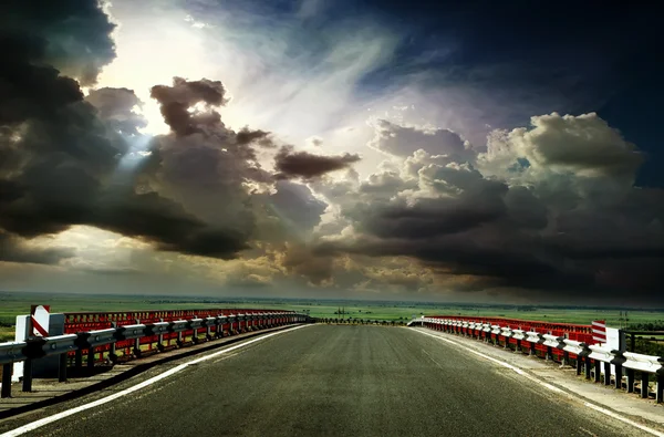 Camino de asfalto con una valla contra el cielo azul — Foto de Stock