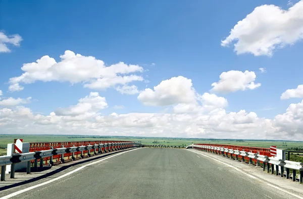 ถนนยางมะตอยที่มีรั้วกับท้องฟ้าสีฟ้า — ภาพถ่ายสต็อก