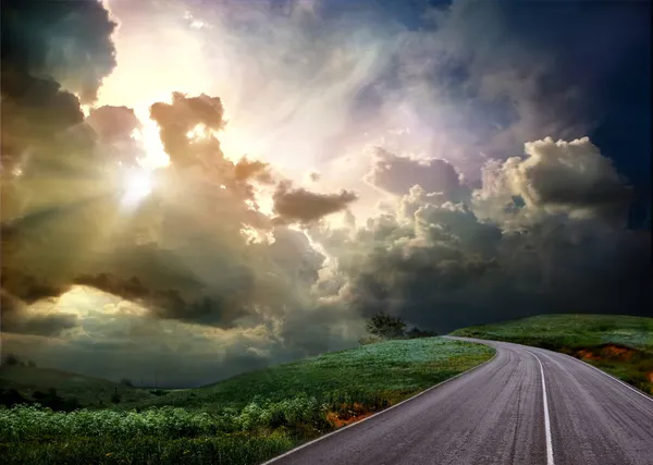 Дорога через луг и бурное небо — стоковое фото