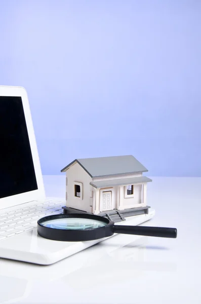 放大镜、 房子模型和具有蓝色背景的笔记本电脑 — 图库照片