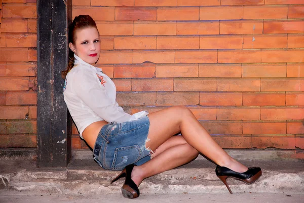 Bella e sexy donna di mezza età, seduta contro un muro di mattoni . — Foto Stock