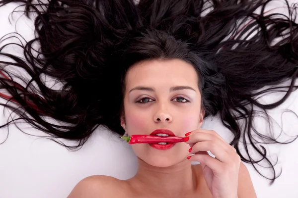 Beautiful woman lying on floor with chili on mouth, studio shot — Stock Photo, Image