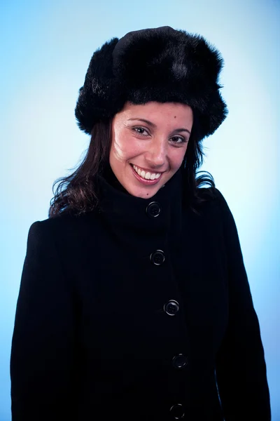 Schöne Frau lächelnd, mit Mütze und Mantel, isoliert auf blauem Hintergrund. Studioaufnahme. — Stockfoto