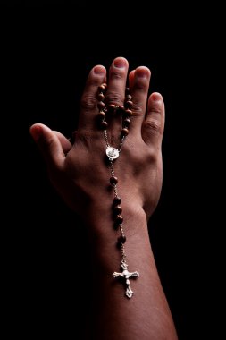 Hands of a young latin men with a crucifix, isolated on black, studio shot clipart