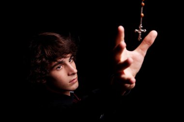 Young men with arm raised, trying to grab a crucifix, isolated on black, studio shot clipart