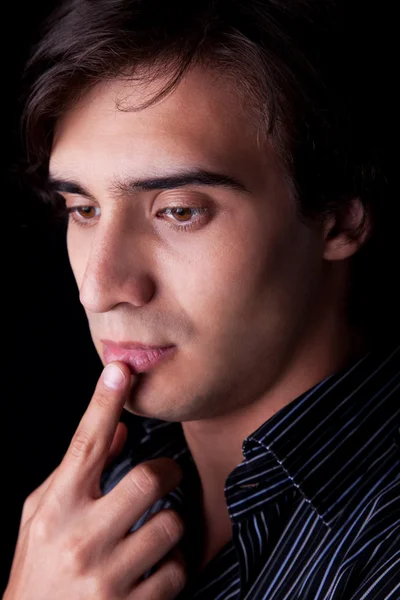 Portrait of a handsome young man thinking, on black background. Studio shot — Stock Photo, Image