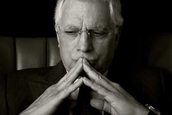 stock image Old businessman seated on a chair, thinking, isolated on black background, Studio shot