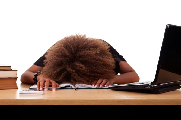 Stressato giovane donna nera, seduto a un tavolo tra libri e laptop su uno sfondo bianco . — Foto Stock
