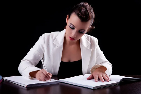 Hübsche Frau am Schreibtisch mit Papieren, schreibend, isoliert auf schwarzem Hintergrund. Studioaufnahme. — Stockfoto