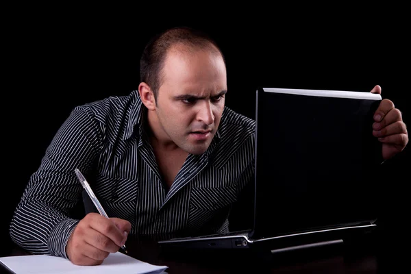 Überraschter Geschäftsmann, der zum Computer blickt und sich Notizen macht, isoliert auf schwarzem Hintergrund. Studioaufnahme. — Stockfoto