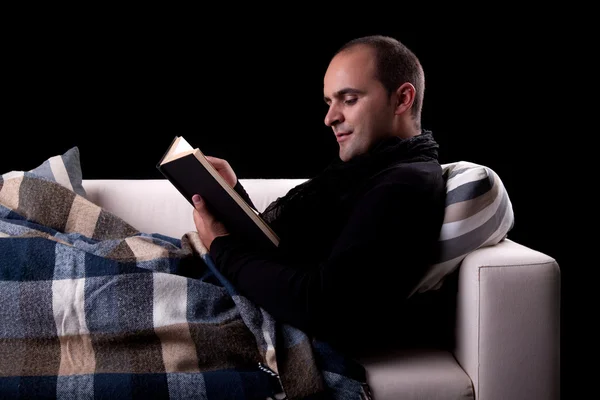 Hombre acostado en el sofá leyendo un libro, aislado en negro, plano de estudio . —  Fotos de Stock