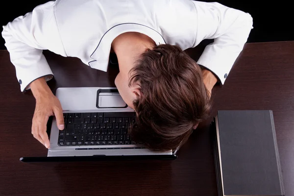 Cansado jovem empresário com a cabeça no computador em um fundo preto. Estúdio — Fotografia de Stock