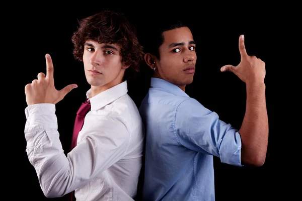 Two young man of different colors, back to back, with hand as an police officer with weapon raised, isolated on black, studio shot — Stock Photo, Image